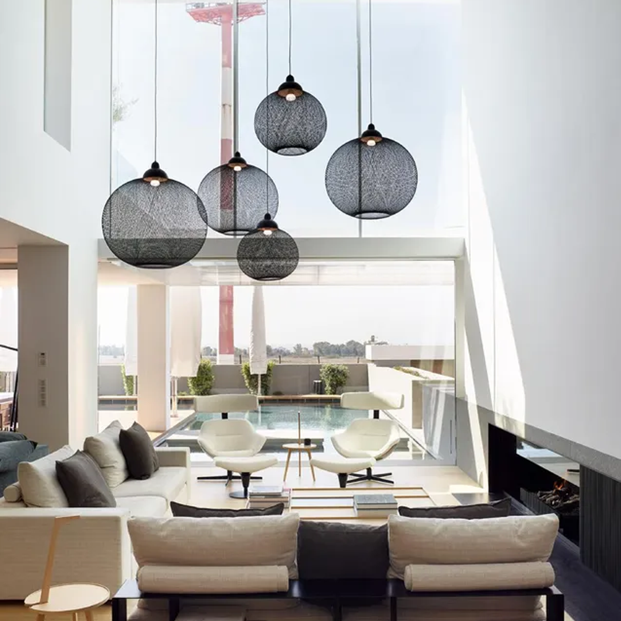 Modern living room with Black Non Random pendant system and a view of a pool.