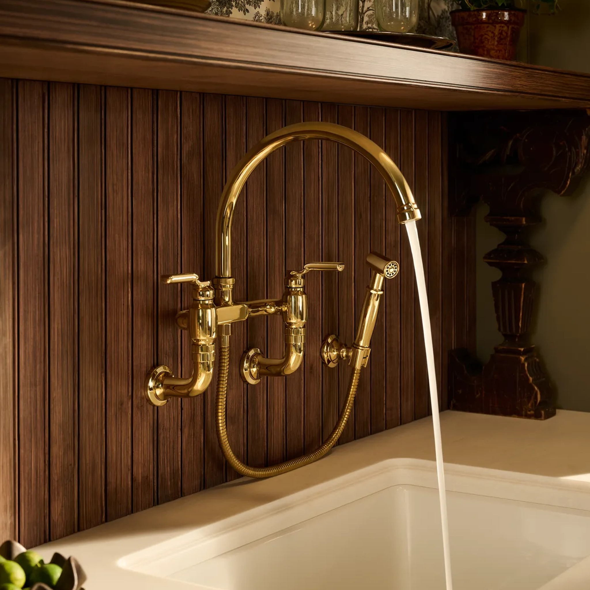 Brizo Faircroft™ bridge faucet with arc spout and side spray in unlacquered brass finish, wall-mount installed in a classic kitchen