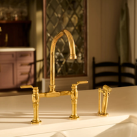 Brizo Faircroft deck-mount bridge faucet  with arc spout and side spray in luxe gold finish mounted with a white undermount sink countertop