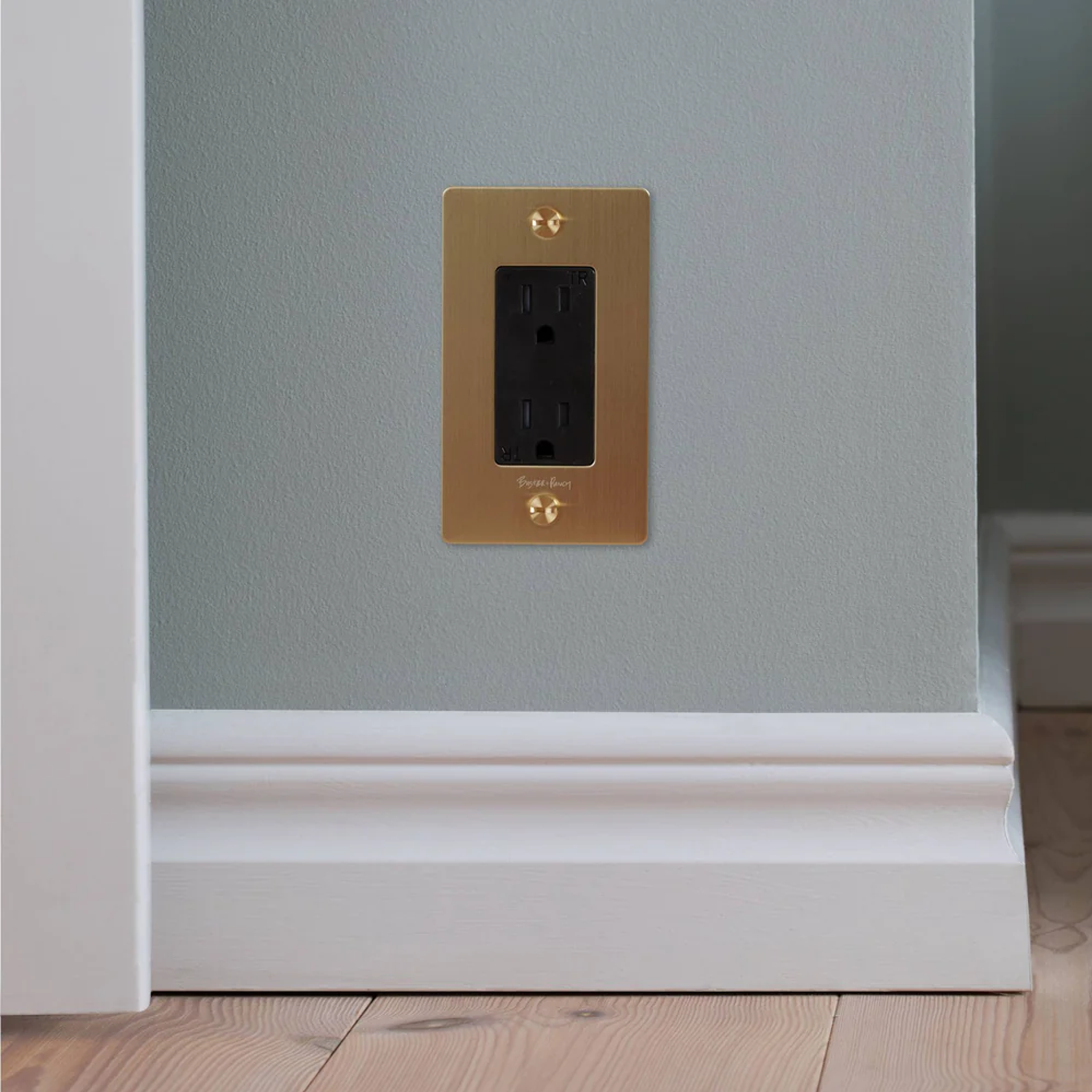 Buster and Punch 1 Gang Cross Outlet in Brass with logo on wall.