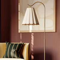A close-up of a modern Eula floor lamp with a curved brass stand and a pleated cream shade in a livingroom.