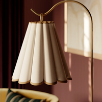 A close-up view of the Eula floor lamp  pleated cream fabric shade hung on a curved gold metal stand.