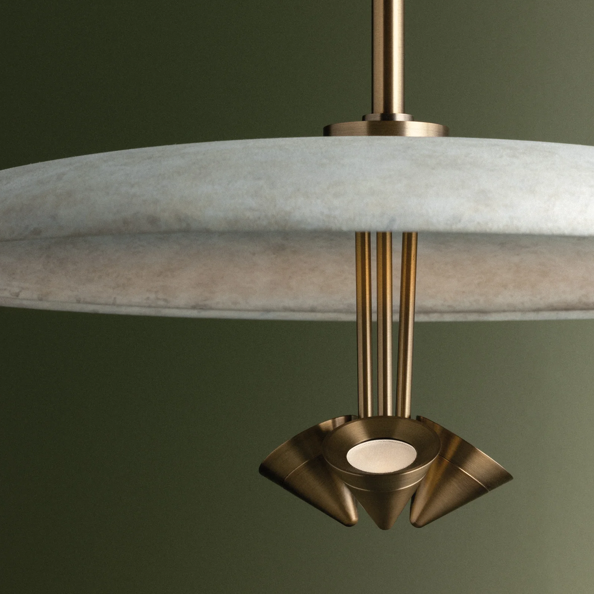 A close-up of a Garth pendant light with a wide, textured light-gray disc shade and a sculptural brass-toned metal fixture below.