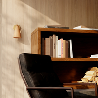 A wood-paneled wall with a Griffith wall sconce by Hudson Valley, a wooden bookshelf holding books and a black leather chair.