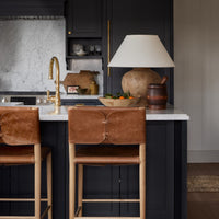 A modern kitchen island with dark navy cabinets, a white marble countertop, and Calabria Table Lamp with a cream shade and a ceramic pot sit on the counter.