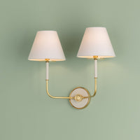 Wedgewood wall sconce with two white lampshades and aged brass arms mounted on pastel green wall