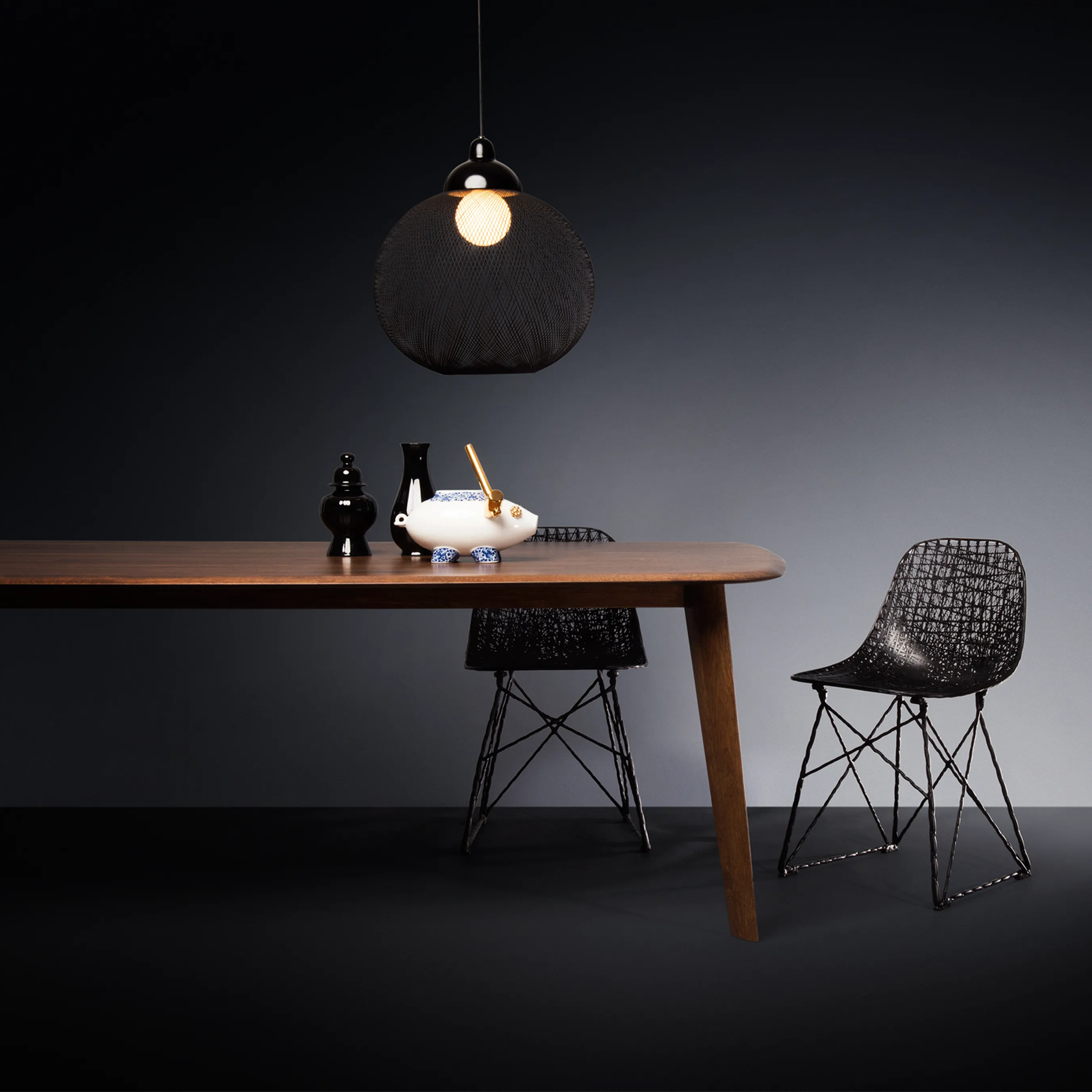 Dining table with two chairs and Non Random pendant light against a dark background