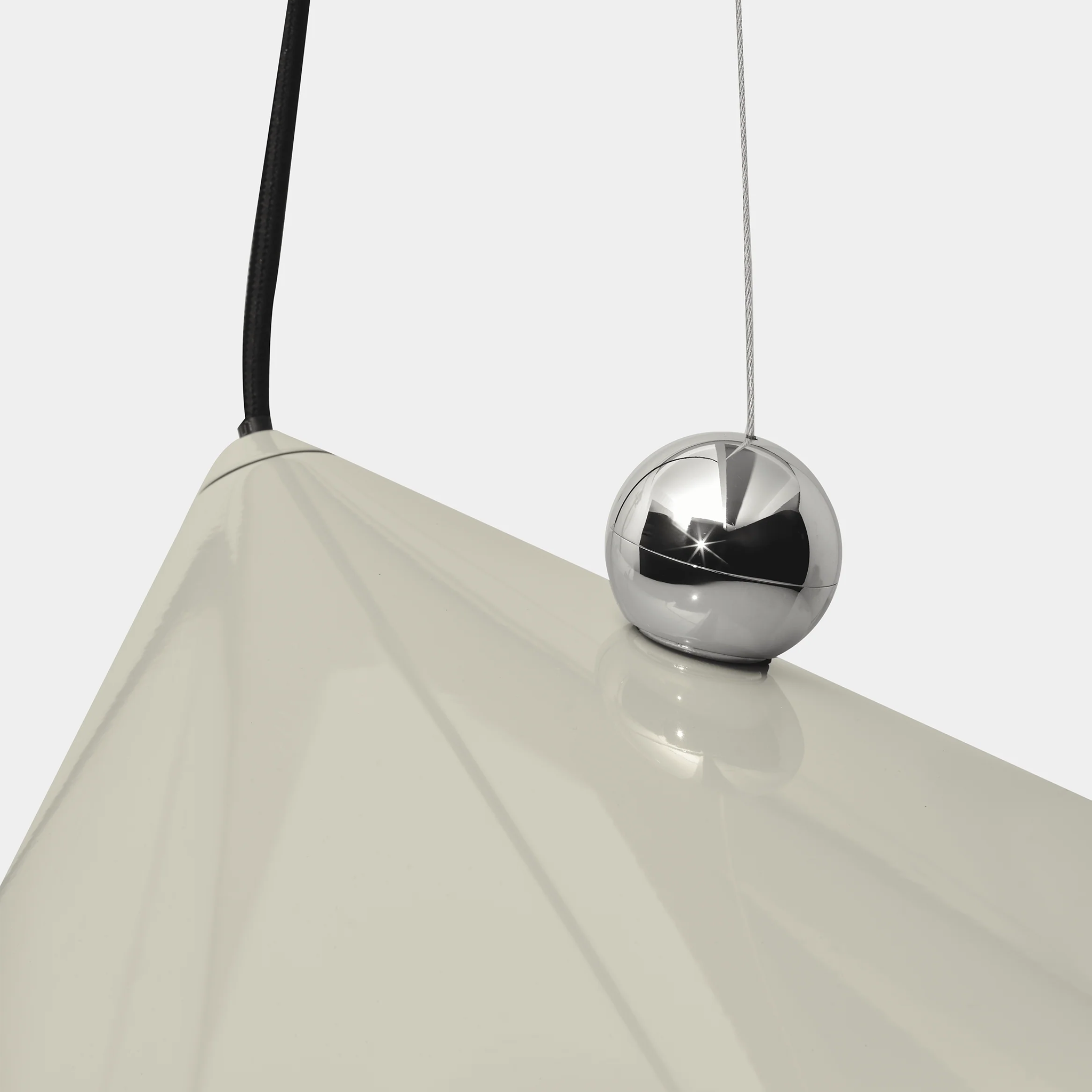 Close-up of a modern Pose pendant light with a glossy cream-colored cone shade and a reflective silver sphere.