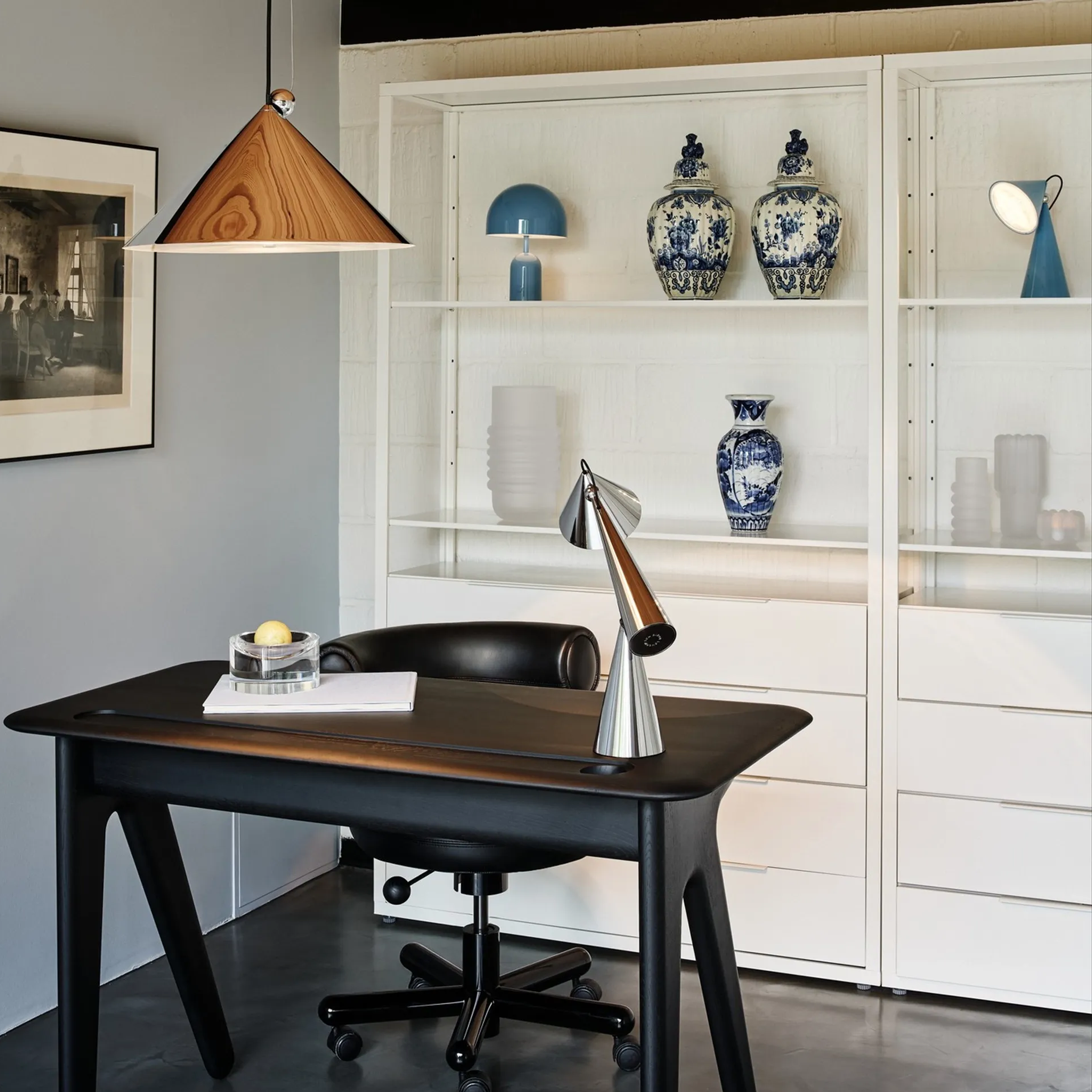 A modern home office setup featuring a dark wood writing desk with a black swivel chair, styled with Tom Dixon Pose table lamp and pendant light.