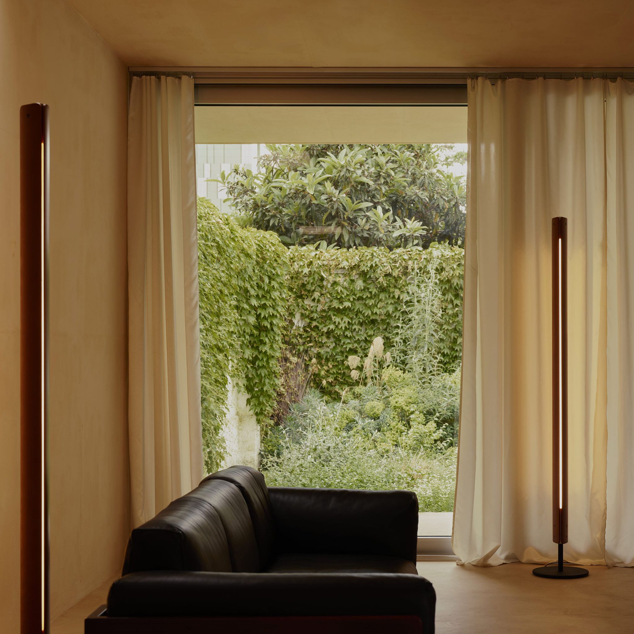 Two Flos Seki-Han floor lamps positioned beside a black leather sofa and floor-to-ceiling curtains in cozy living room.