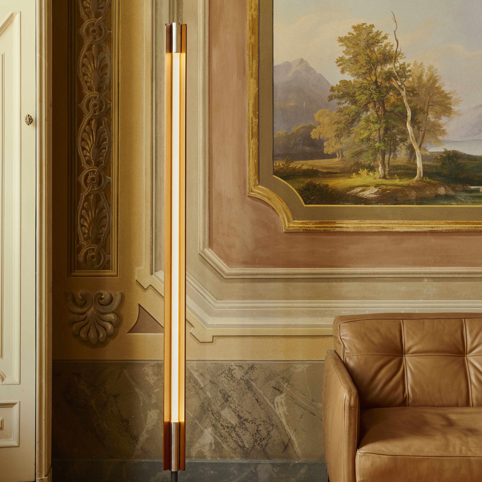 Flos Seki-Han floor lamp positioned beside a tan leather armchair in an elegant interior featuring ornate wall moldings, marble wainscoting, and a framed landscape painting.