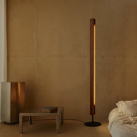 Flos Seki-Han floor lamp in a warm wood finish, beside a low metal table in a minimalist bedroom.